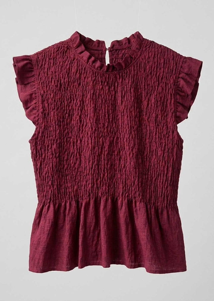 A burgundy smocked blouse with ruffled cap sleeves, a high ruffled collar, and a gathered peplum hem, shown against a light gray background.