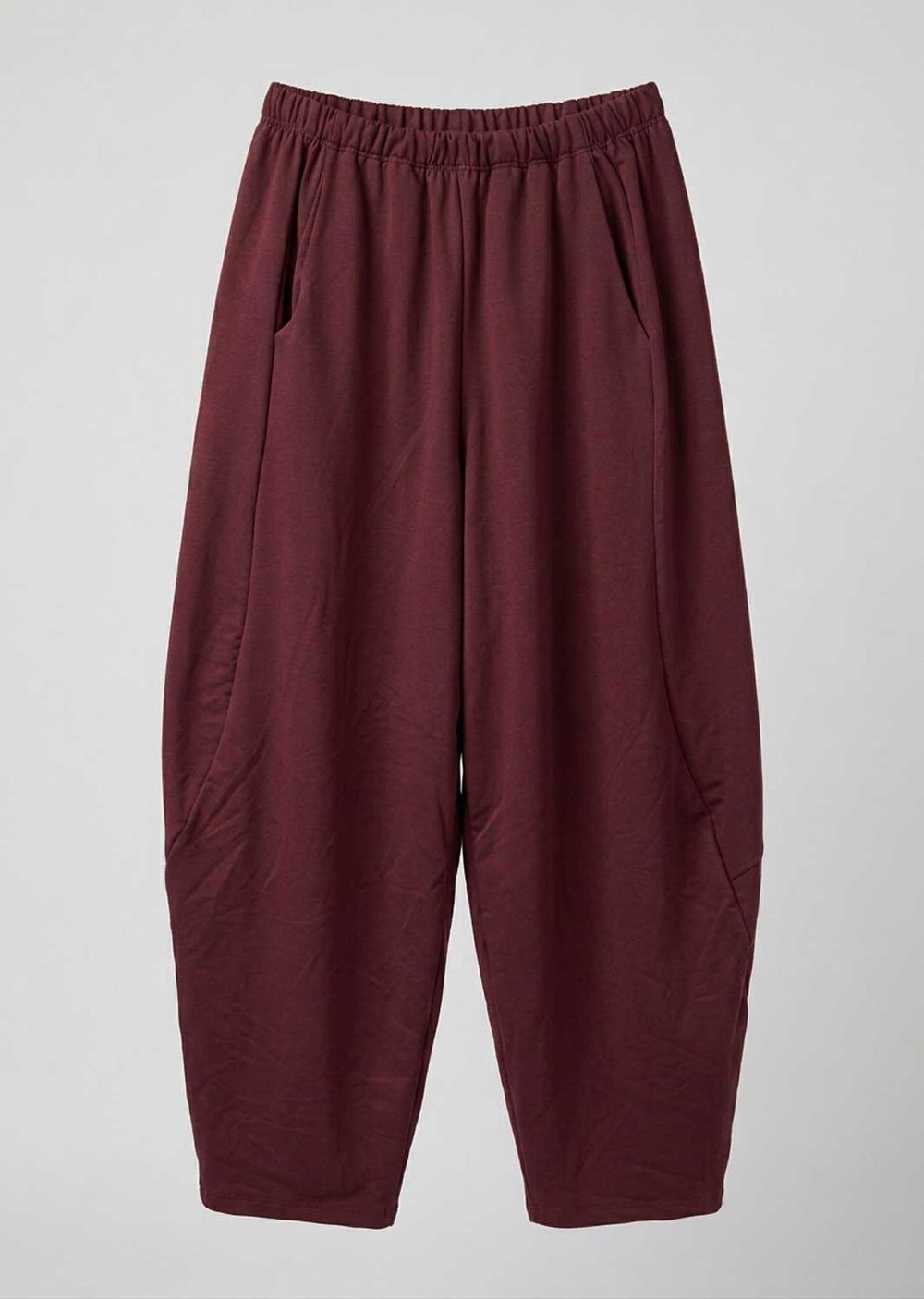A pair of loose-fitting, wide-leg pants in a deep burgundy color, featuring an elastic waistband and side pockets, shown against a neutral light gray background.