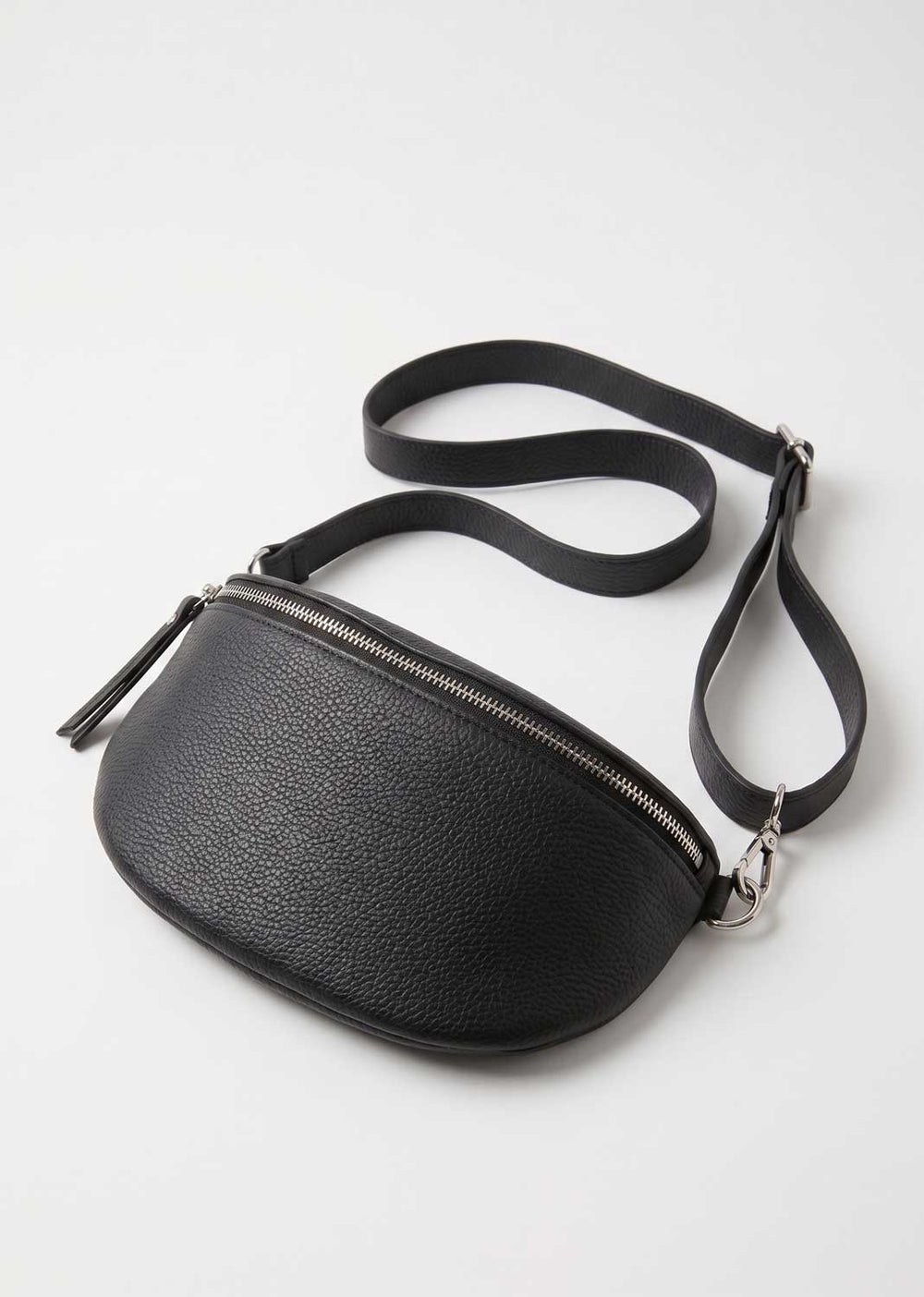 A black pebbled leather crossbody bag with a curved, crescent-like silhouette, a top zipper with a zipper pull, and a matching adjustable shoulder strap, shown on a light gray background.