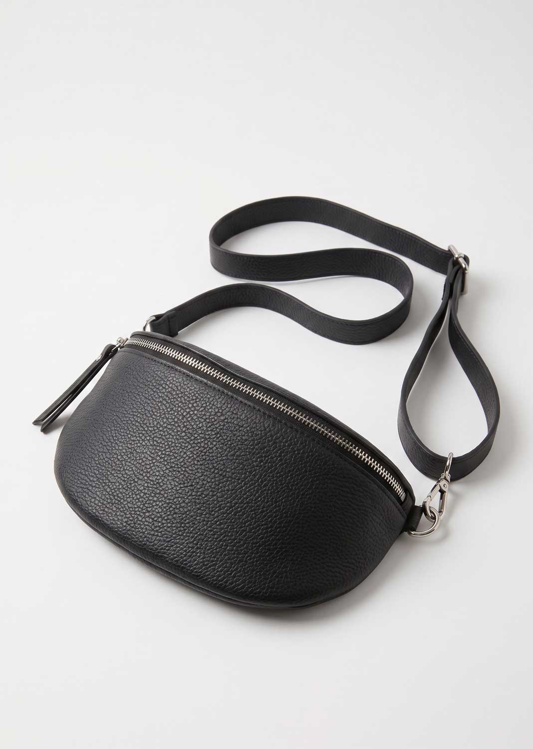 A black pebbled leather crossbody bag with a curved, crescent-like silhouette, a top zipper with a zipper pull, and a matching adjustable shoulder strap, shown on a light gray background.