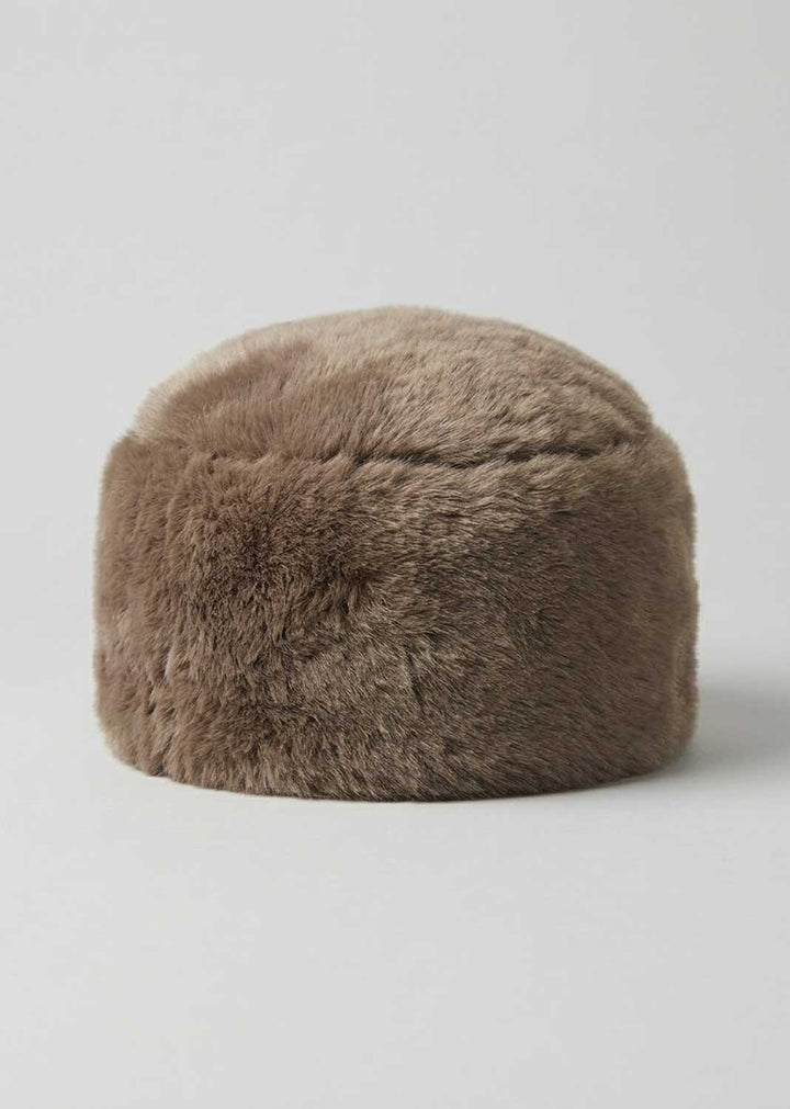 A round, low-profile faux fur hat or stool in a warm taupe-brown color, photographed against a neutral light gray studio background.