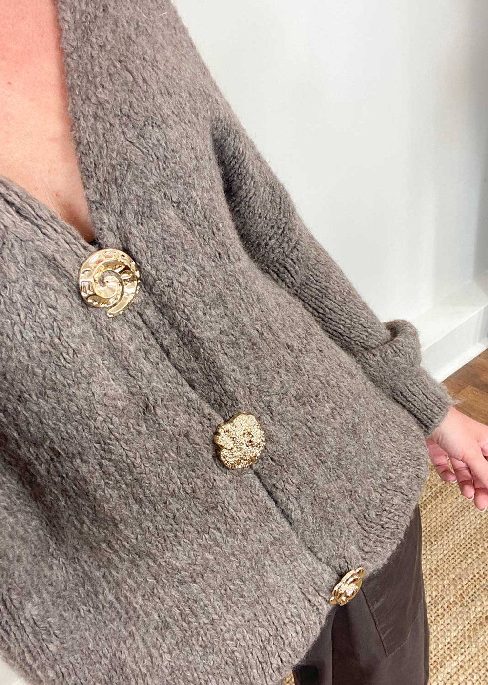 Close-up of a gray textured garment with gold buttons on a neutral background