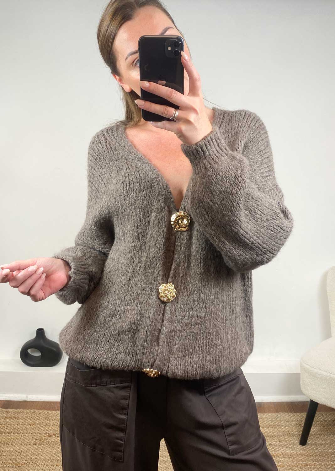 Person wearing a taupe cardigan with gold buttons 