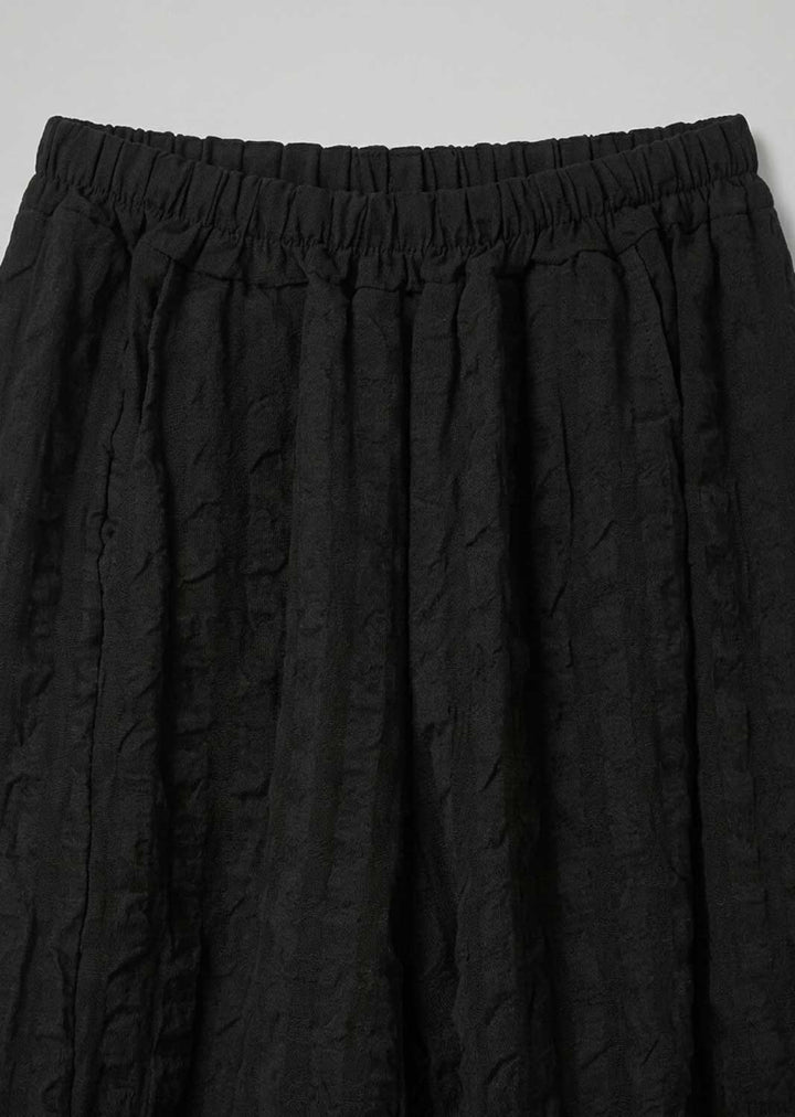 Close-up of black textured pleated fabric with an elastic waistband, shown against a light gray background.