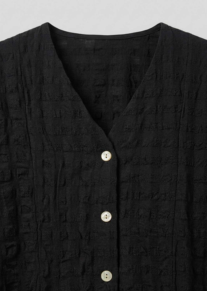 Close-up of a black textured button-front top with a V-neck and light-colored buttons, shown against a plain light gray background.