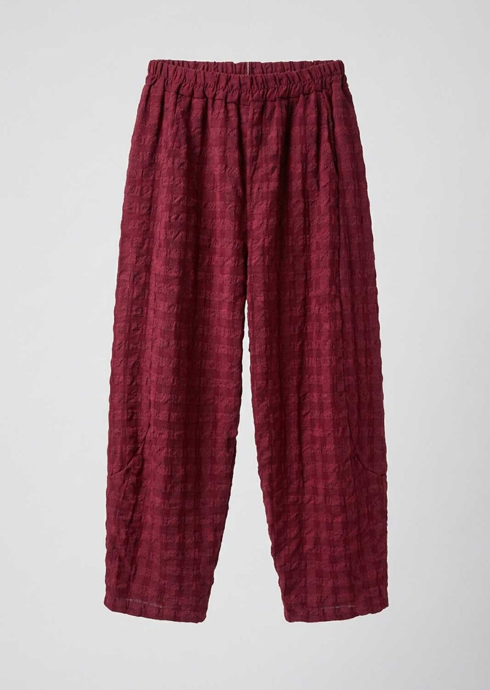 A pair of loose, pleated trousers in a deep burgundy red fabric, displayed flat against a light gray background.