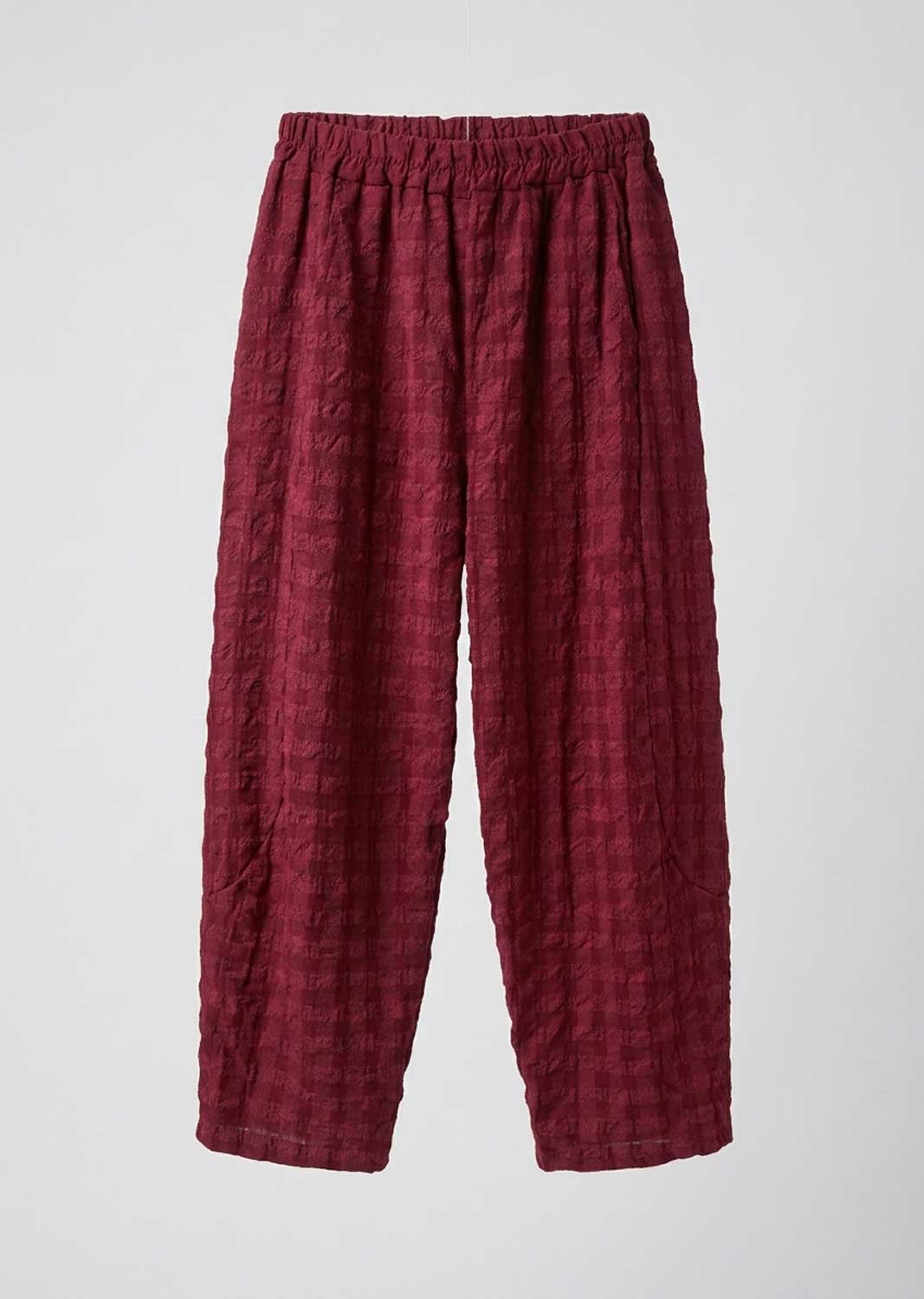 A pair of loose, pleated trousers in a deep burgundy red fabric, displayed flat against a light gray background.