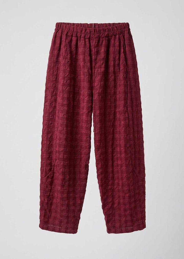 A pair of loose, pleated trousers in a deep burgundy red fabric, displayed flat against a light gray background.