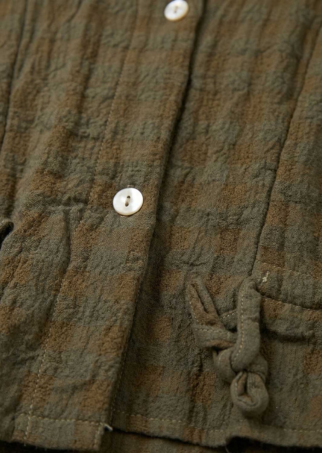 Close-up of a textured olive green crinkled fabric garment with white buttons and a matching fabric drawstring knot.