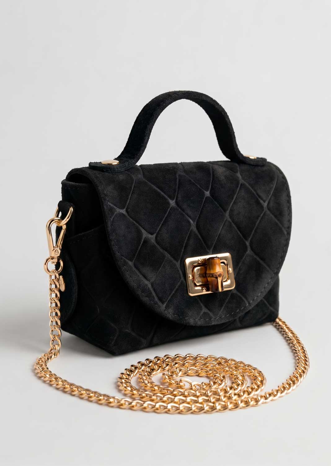 Black croc suede handbag with a top handle, gold-tone turn-lock closure, and a long gold chain strap, photographed on a light gray background.