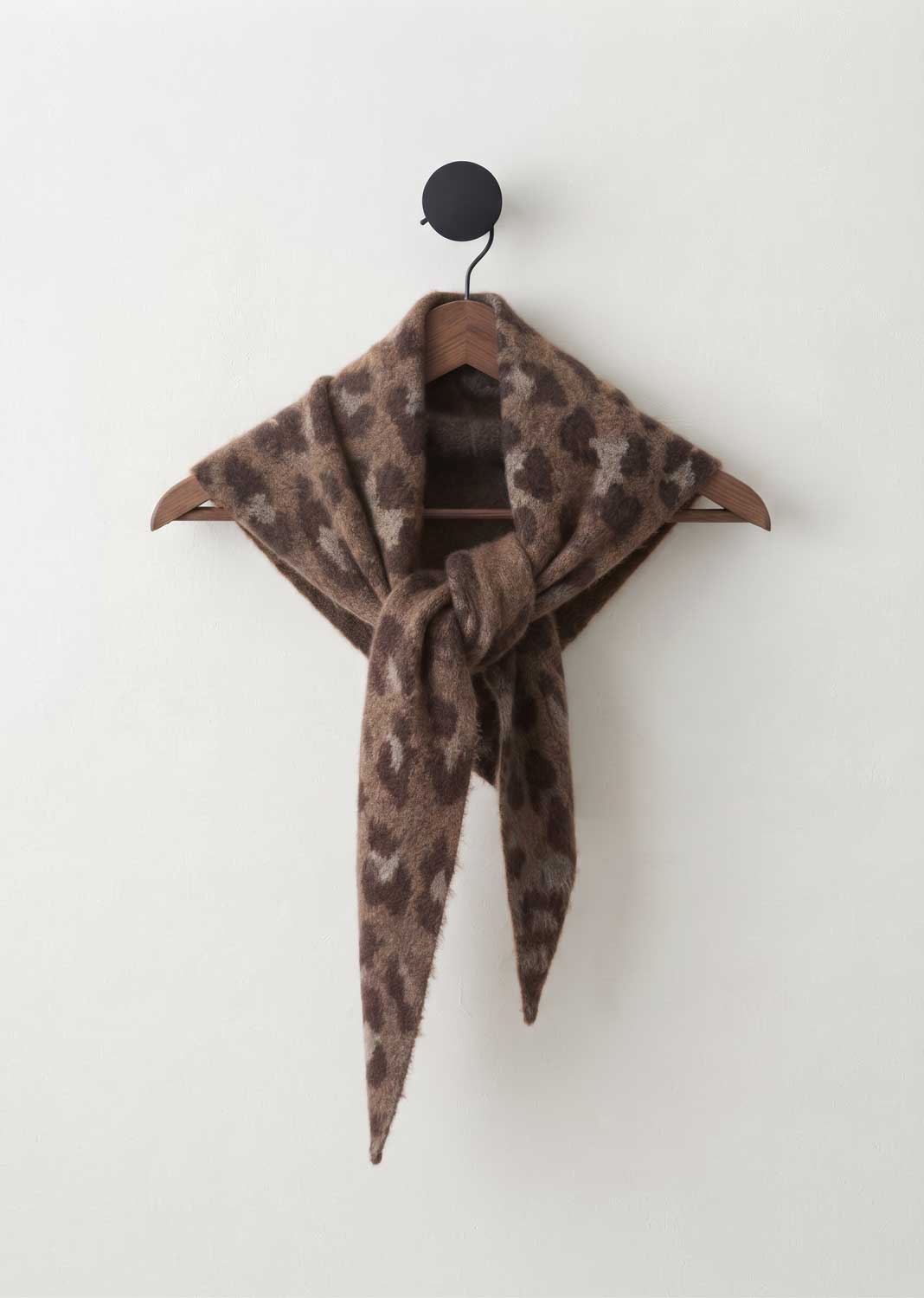 A brown and beige leopard-print scarf tied in a knot on a wooden hanger against a plain off-white wall.