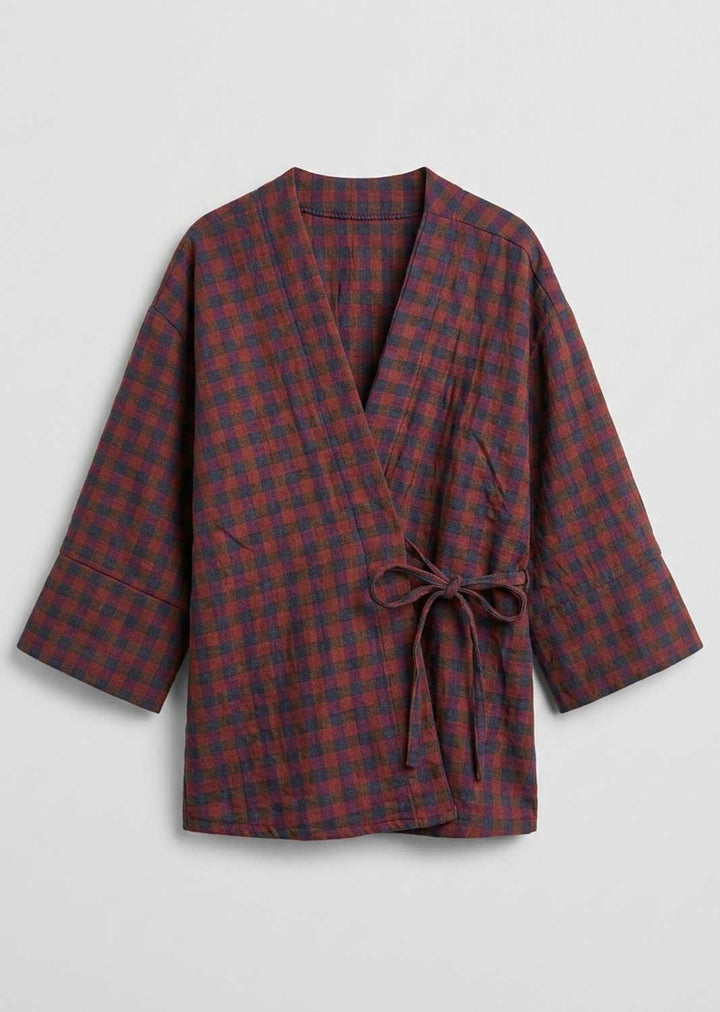 A long-sleeved wrap robe with a red and dark blue plaid pattern, featuring a tie belt at the waist, displayed against a light gray background. 