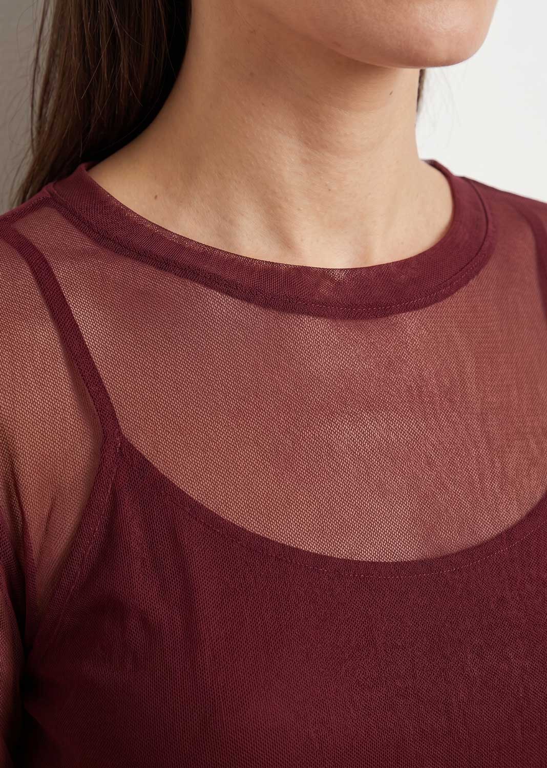Close-up of a model wearing a burgundy sheer mesh top layered over a camisole.