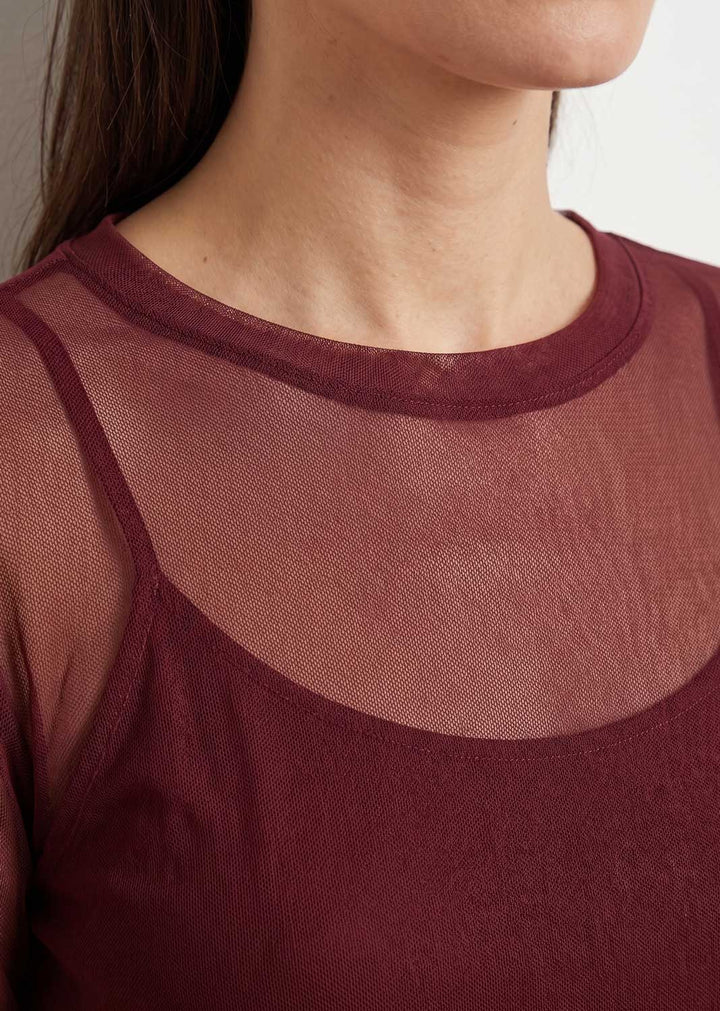 Close-up of a model wearing a burgundy sheer mesh top layered over a camisole.