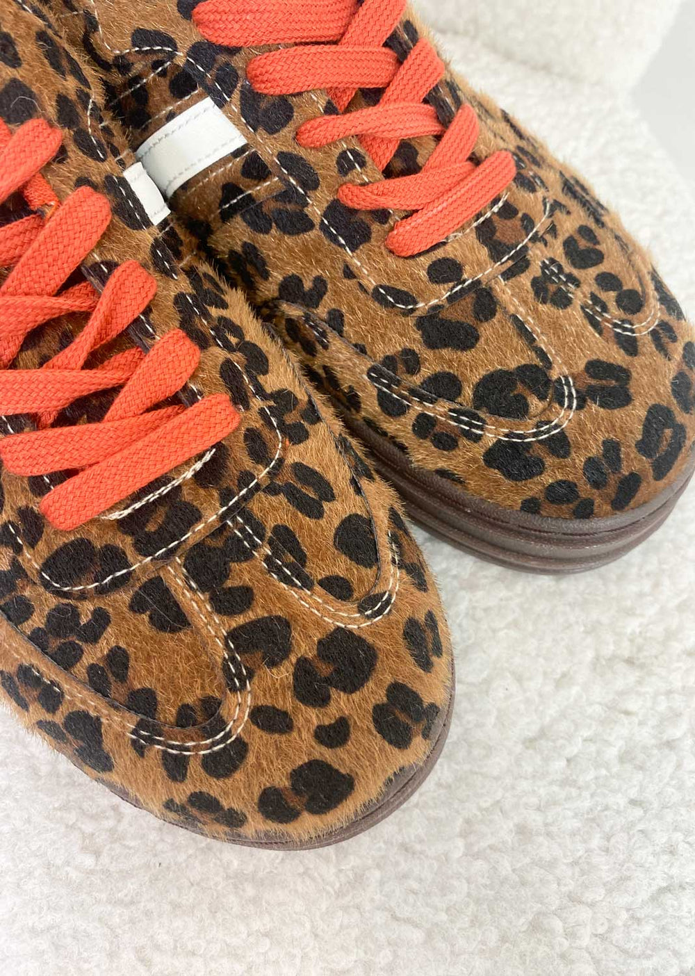 Leopard print shoes with orange laces on a light gray background