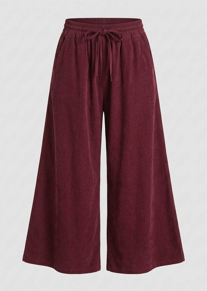 A pair of wide-leg pants in a deep burgundy corduroy fabric, featuring an elastic waistband with a matching drawstring, shown against a light gray background.