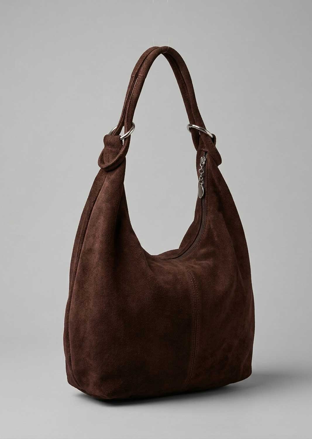 A dark brown suede hobo shoulder bag with silver-tone hardware, shown on a neutral gray background.