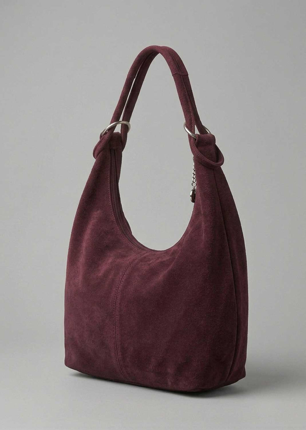 A slouchy hobo shoulder bag in deep burgundy suede, featuring knotted details at the strap attachments and silver-tone hardware, set against a plain gray studio background.