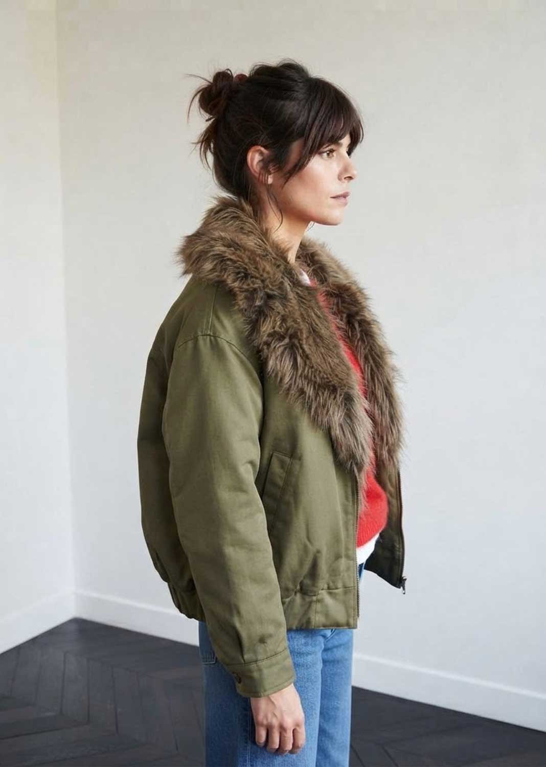 A woman in profile wearing an olive green bomber jacket with a large brown faux-fur collar,