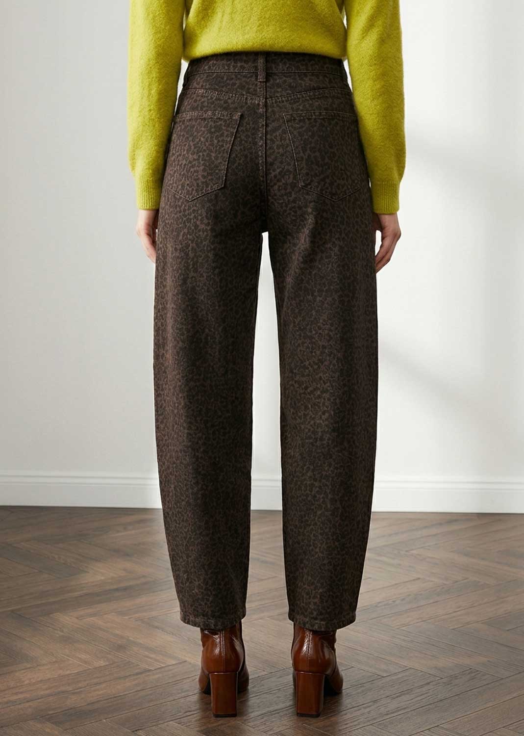 A person shown from the back wearing high-waisted brown barrel leg jeans, a bright yellow-green sweater, and brown ankle boots in an indoor room with a wood floor and white wall.