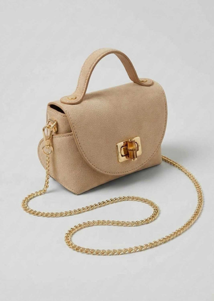 A beige suede mini handbag with a top handle, gold-tone turn-lock clasp, and a gold chain shoulder strap, displayed on a light gray background.