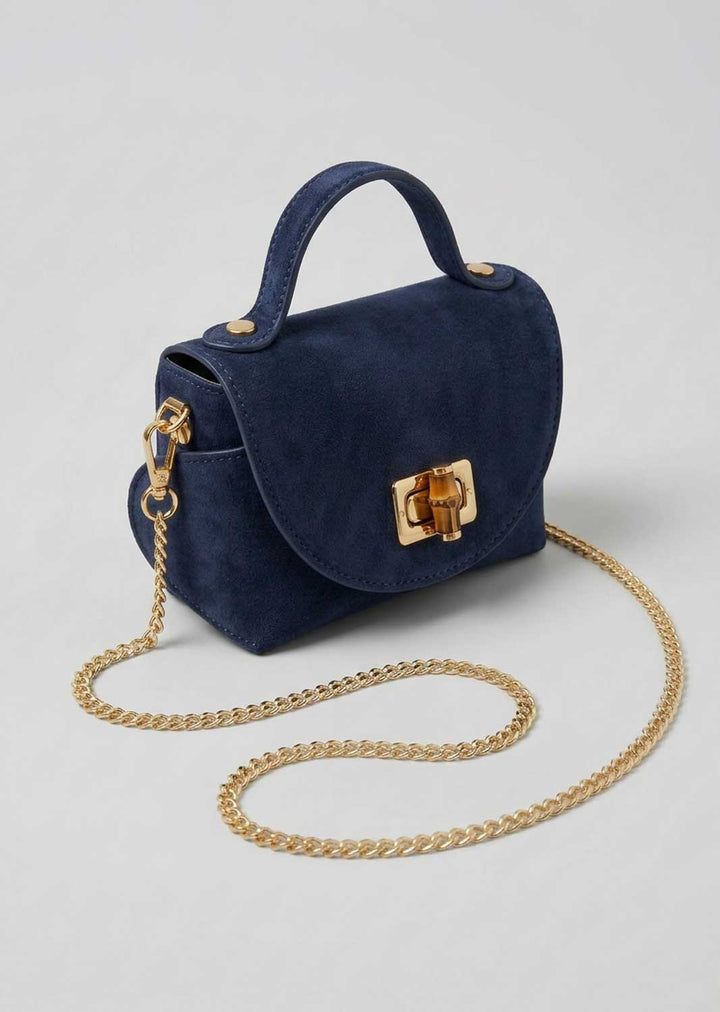 A dark green suede top-handle handbag with a gold-tone turn-lock clasp and a gold chain shoulder strap, displayed on a light gray background.