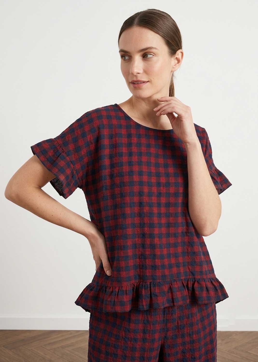A woman modeling a matching two-piece plaid pajama set with a red and navy blue checkered pattern, featuring a short-sleeve top with ruffled edges and matching pants.