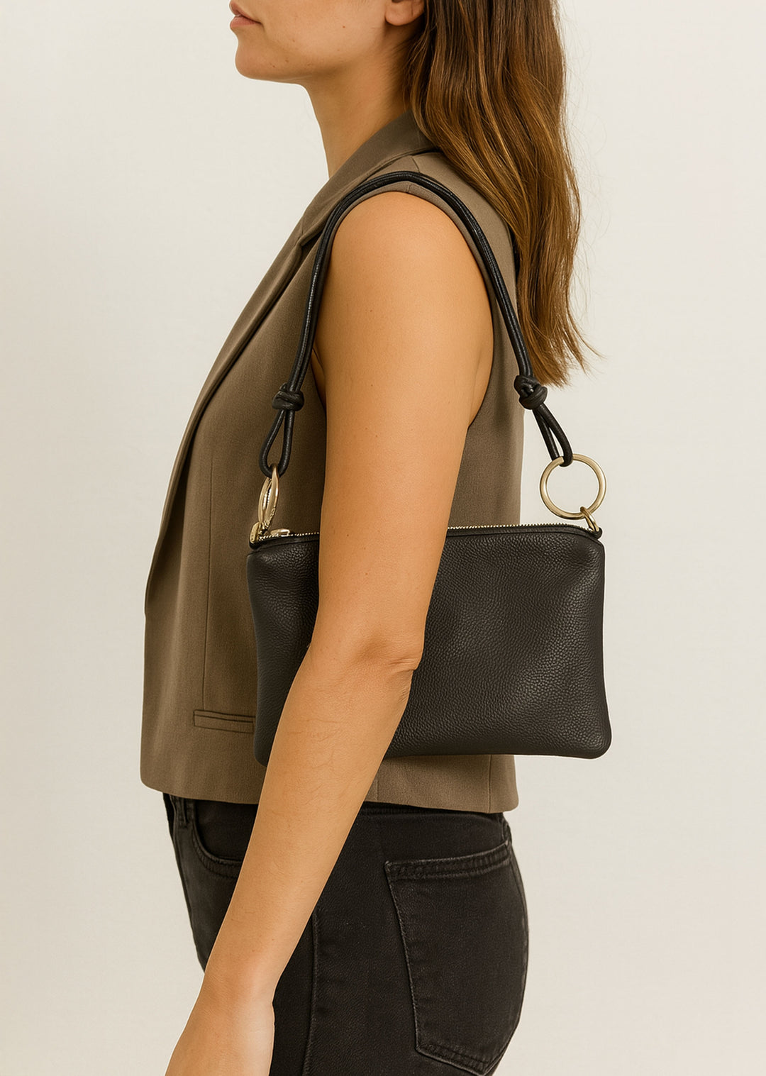 Woman with a black leather handbag with gold ring  hardware against a neutral background