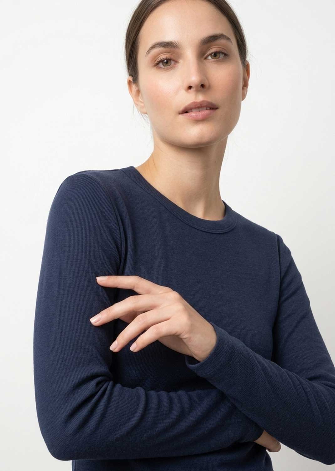 A woman wearing a dark navy blue long-sleeve crewneck knit top, posed against a clean white studio background.