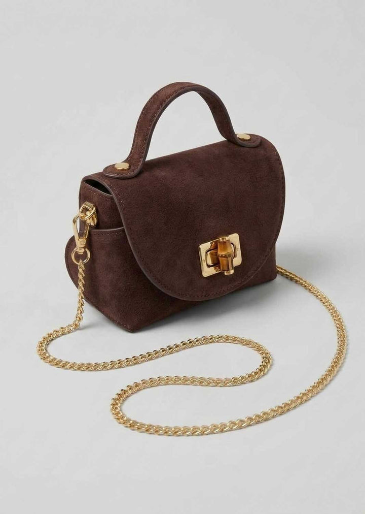 A dark brown suede top-handle handbag with a gold-tone chain strap and a gold clasp, shown on a light gray background.